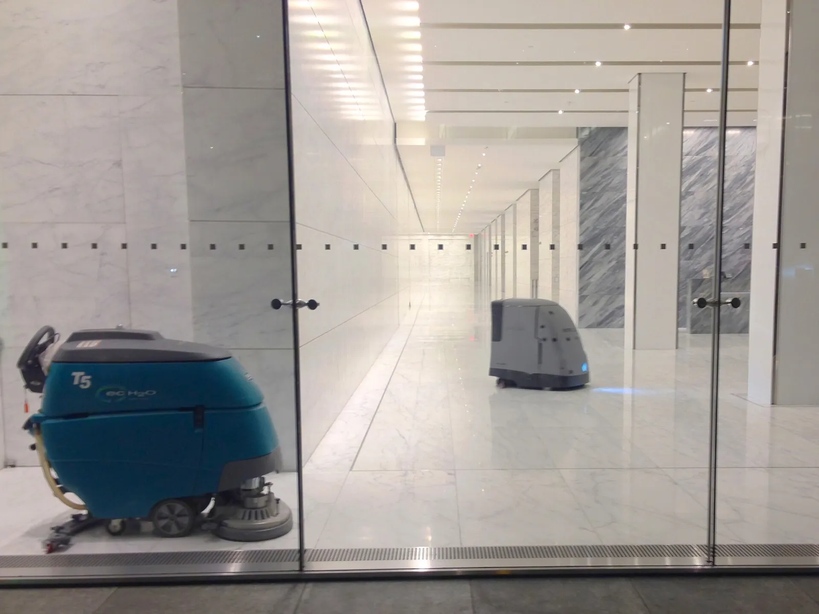 A walk-behind floor scrubber crossing a marble office lobby
