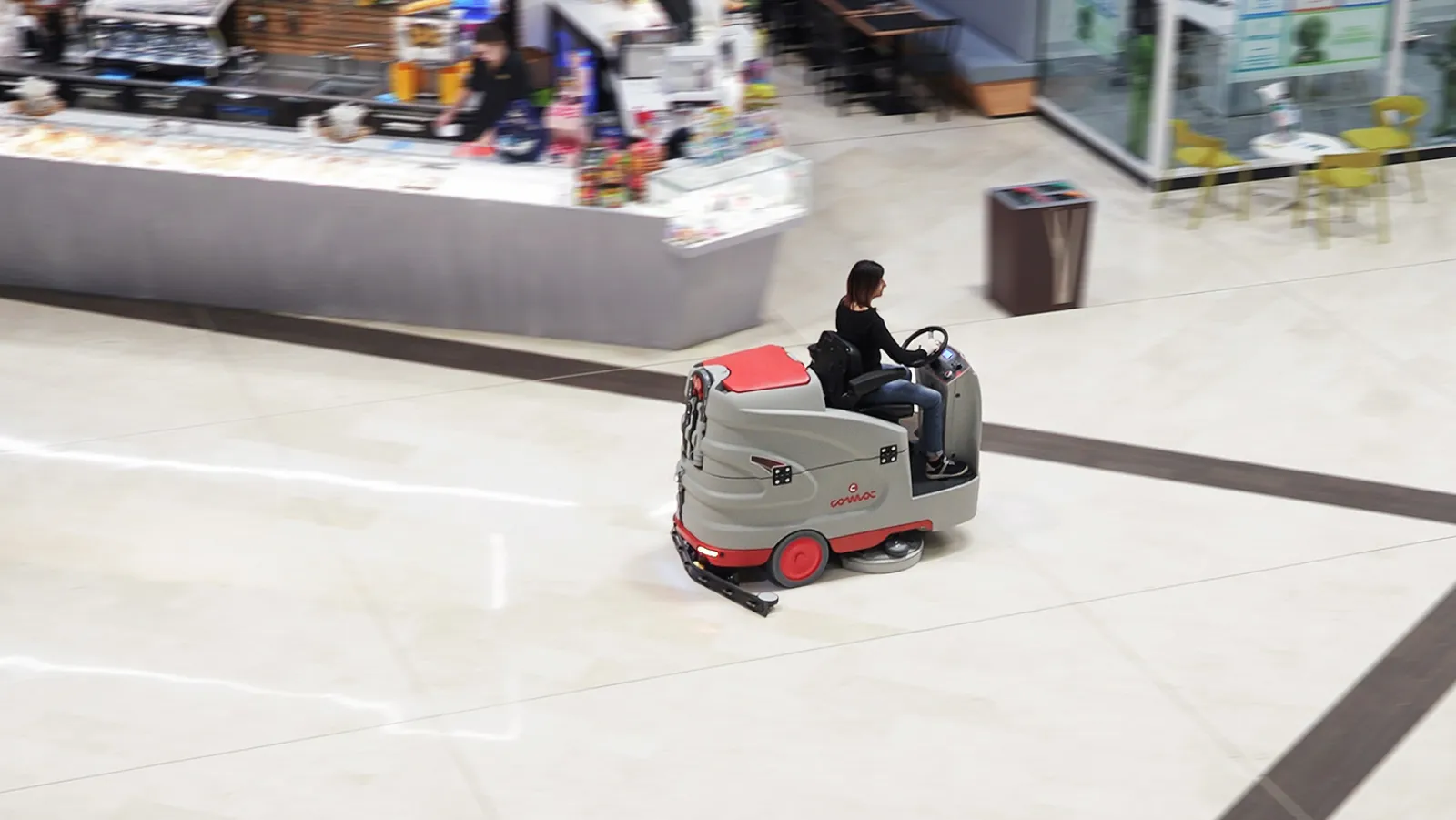 An operator on a ride-on floor scrubber in a shopping mall