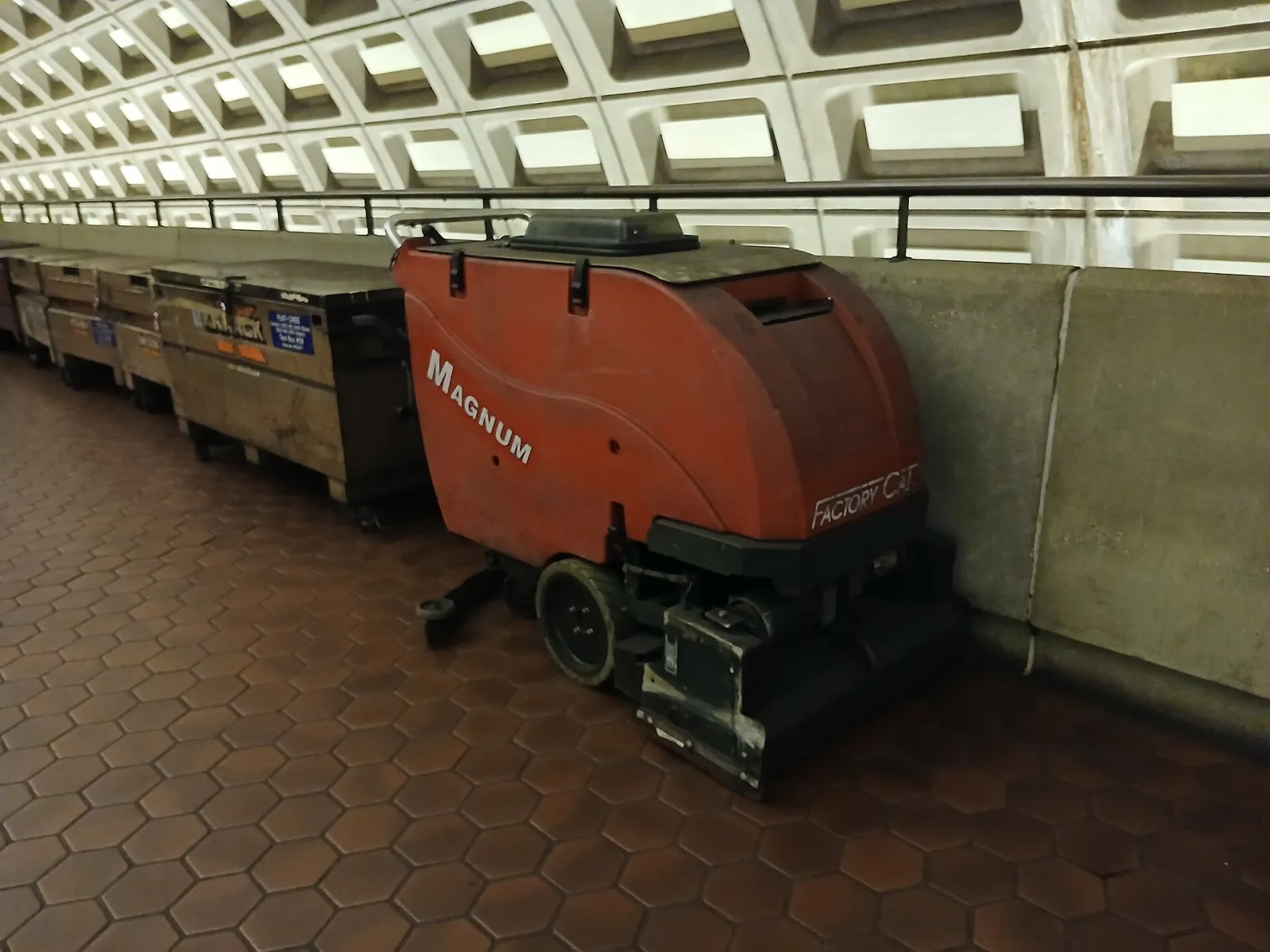 A walk-behind floor scrubber parked on the mezzanine of a transit station